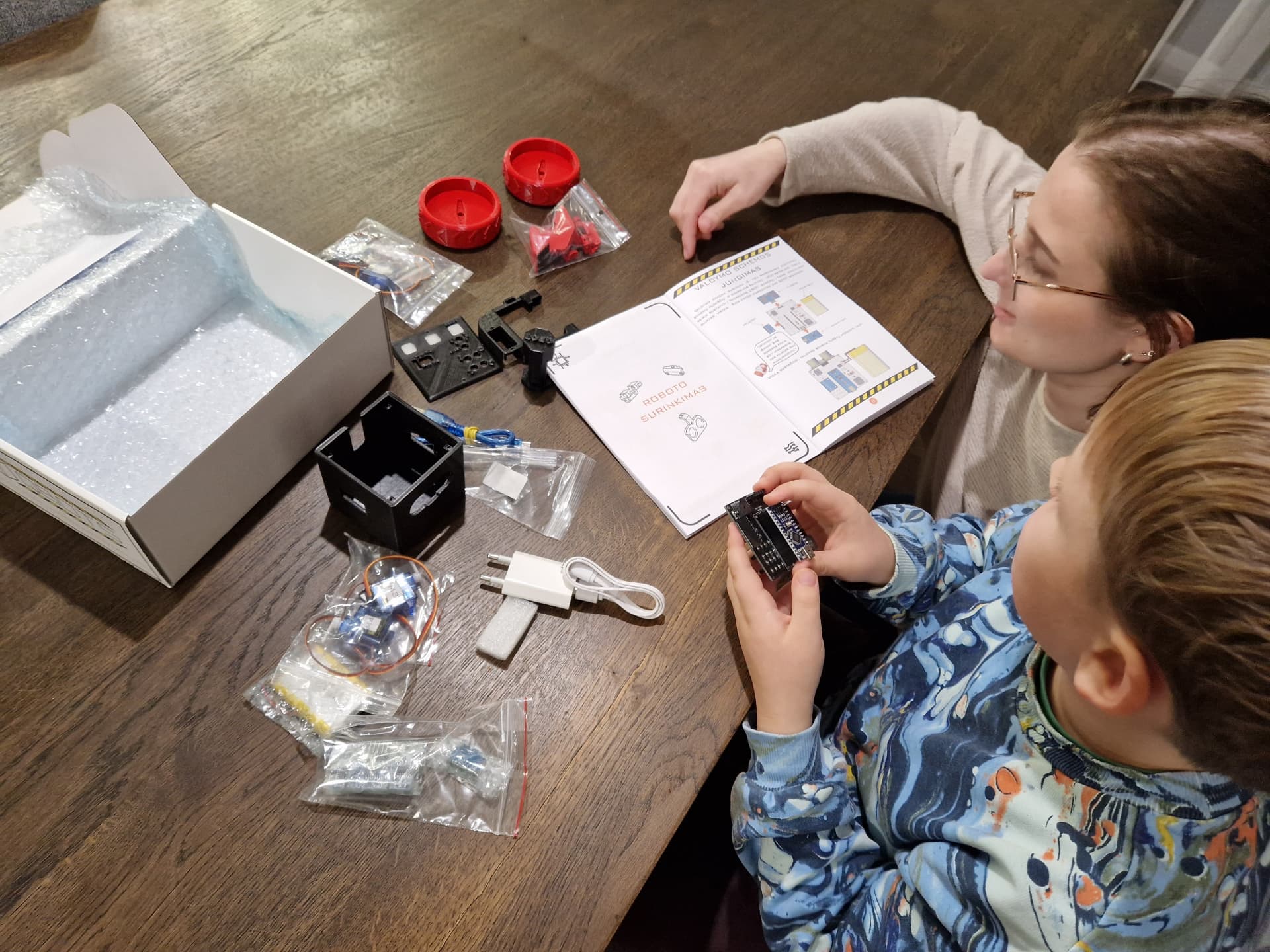 Vaikas su mama išpakuoja QBOT roboto rinkinį