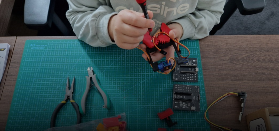 Vaikas surenka QBOT roboto detales ant darbo kilimėlio